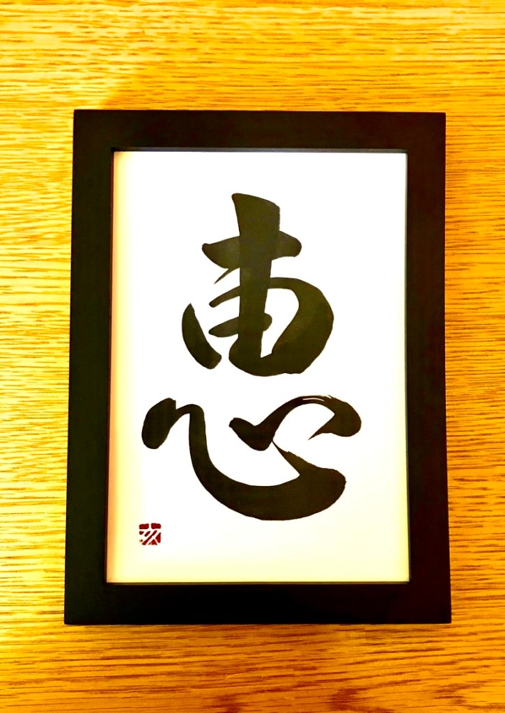 A Japanese calligraphy work of 1 character, black ink on white paper, in a black frame.