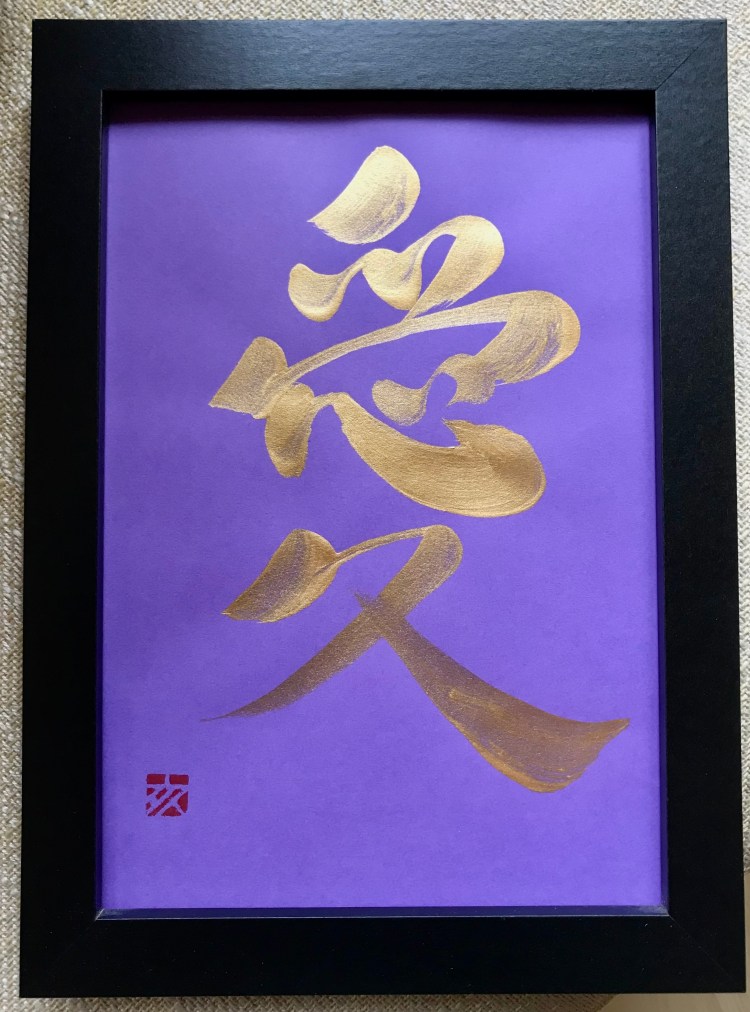 A Japanese calligraphy artwork of 1 character. The ink is gold, and the paper is purple. It is in a black frame.