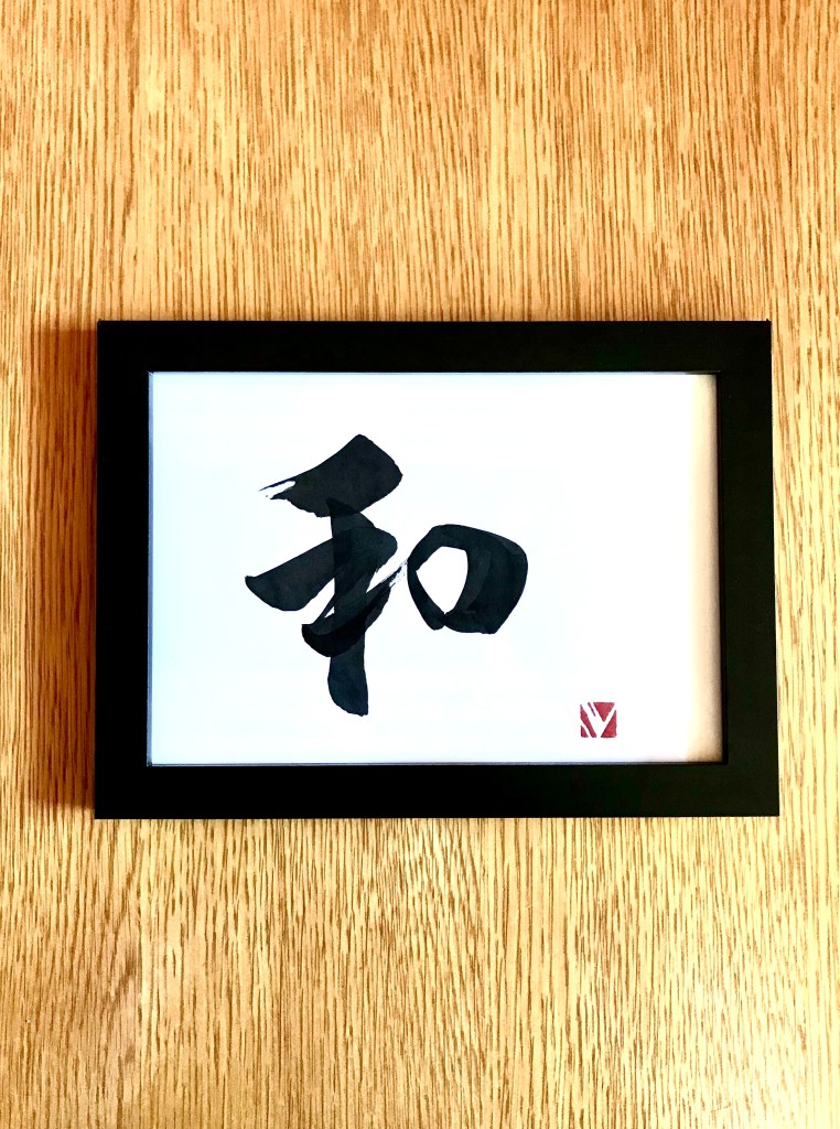 A Japanese calligraphy work of 1 character, black ink on white paper, in a black frame.
