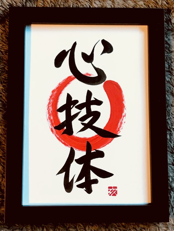 A framed Japanese calligraphy work with the characters "heart", "skill" and "body".