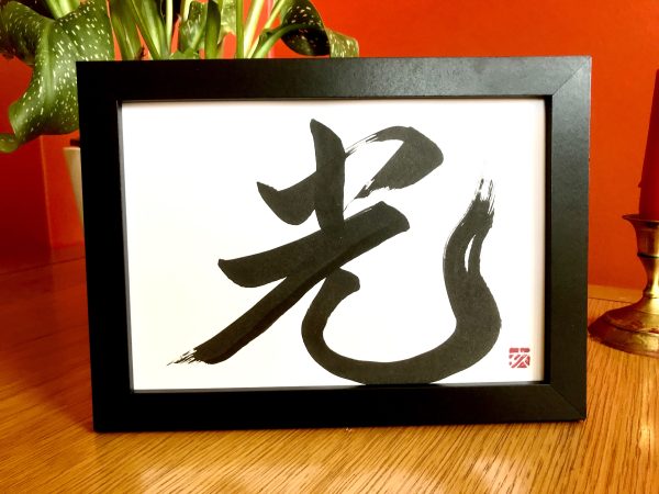 A framed calligraphy artwork of the Japanese character for "light".