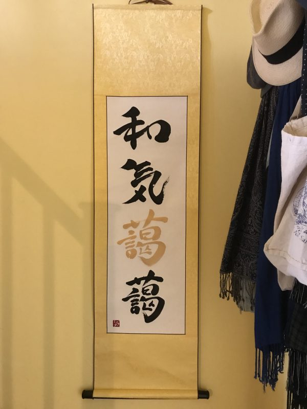 A yellow hanging scroll of 4 Japanese characters in black and gold ink.