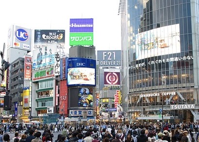 The famous crowded crossing in Shibuya, Tokyo. There are many shop signs and company logos on the buildings in the background.