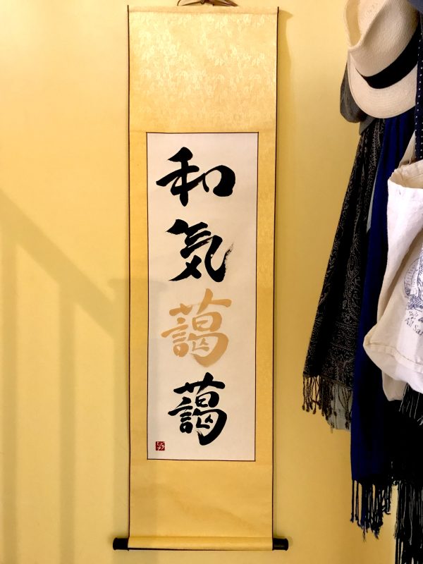 A 4-character Japanese calligraphy work on a yellow hanging scroll, the ink is black and gold.
