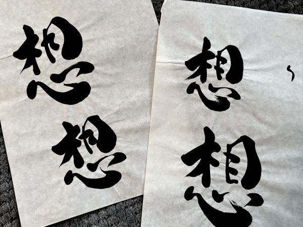 Two pieces of Japanese calligraphy paper with multiple versions of the same kanji written on them,