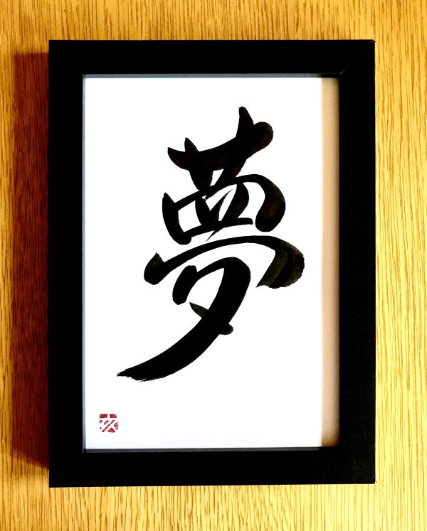 A Japanese calligraphy work of the character for "dream", black ink on white card, with a black frame.