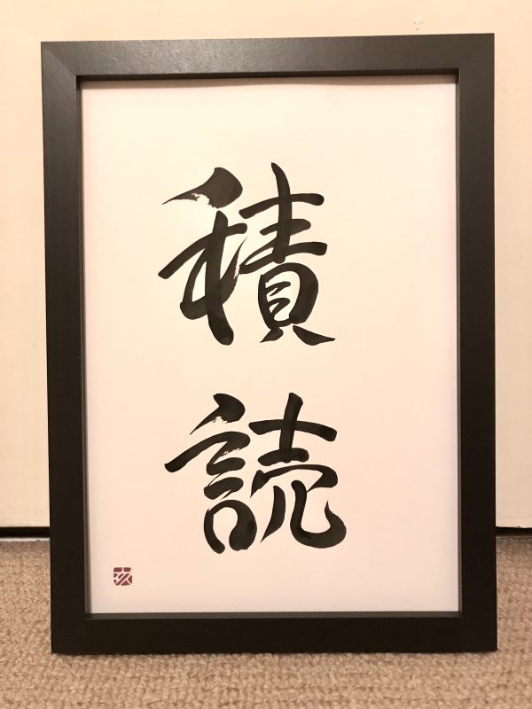 A 2-kanji Japanese calligraphy work, black ink on white card, with a black frame.