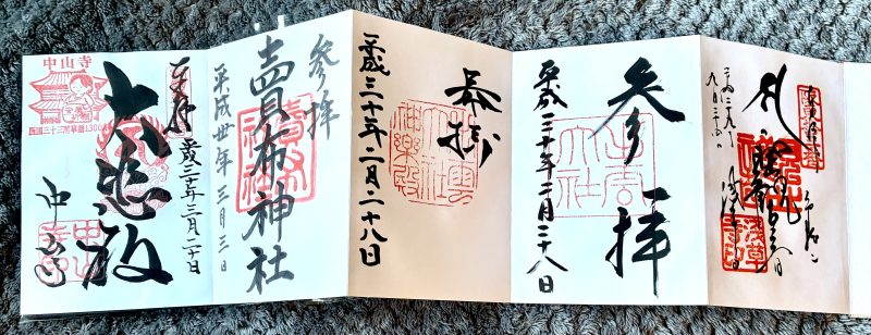 A folded-out book of white pages covered in black Japanese calligraphy and red ink stamps